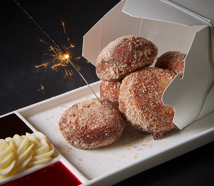 Cinnamony doughnuts with sparkler, served with a side of dipping sauce and sliced apples.