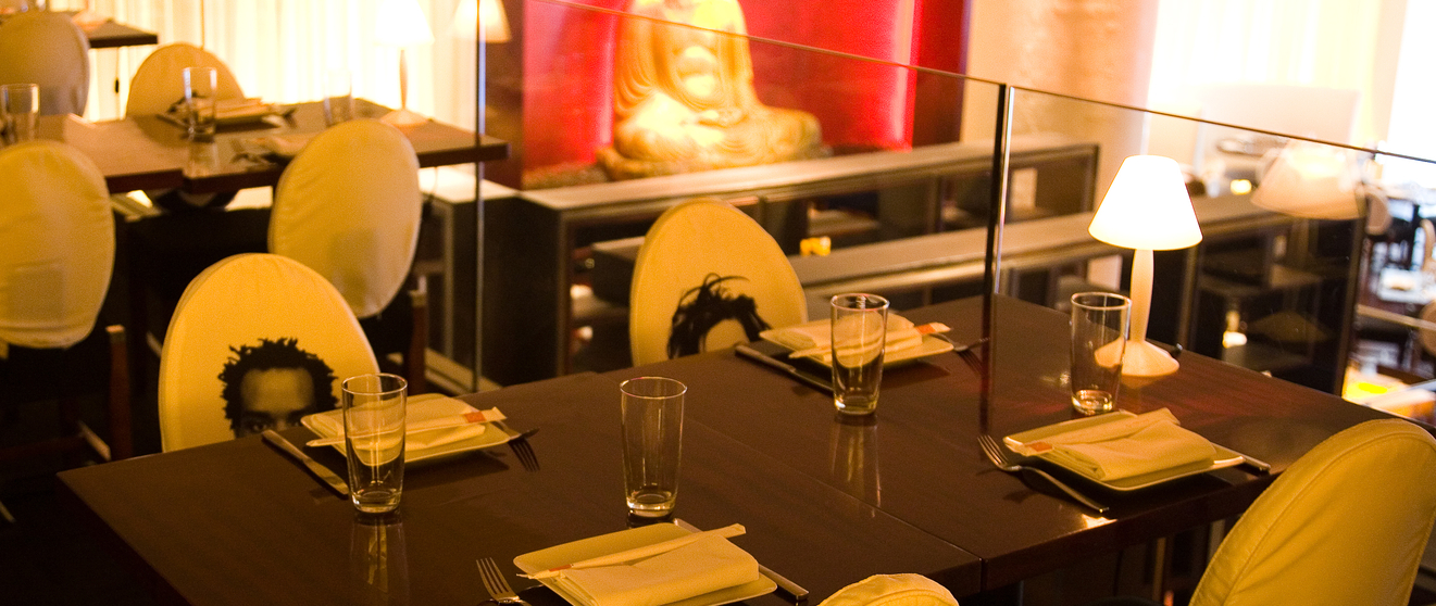 Elegant dining room with yellow chairs, black tables, and a red-lit Buddha statue in the background.